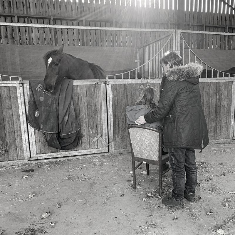 Black and white picture of a lady on a chair in a stable