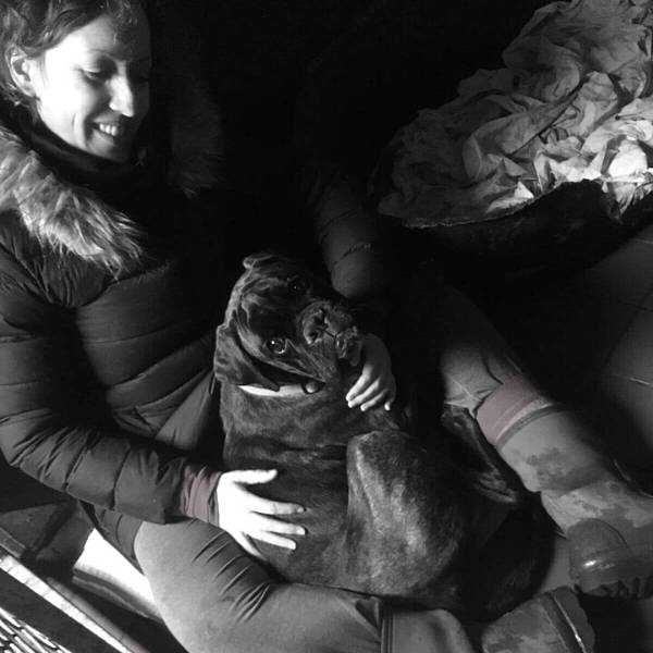 Black and white picture of Ali with a black dog in her lap who is looking up at the camera